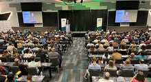 A speaker stands at a podium addressing a large audience.