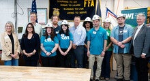 A group of students stand with government leaders wearing mining hats.