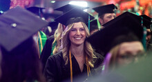 A graduated student wearing cap and gown smiles after receiving her diploma.