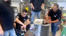 A group of students learn how to repair an air conditioning unit from an instructor.