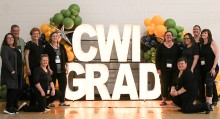 Staff posing in front of a CWI grad light and balloons sign at commencement