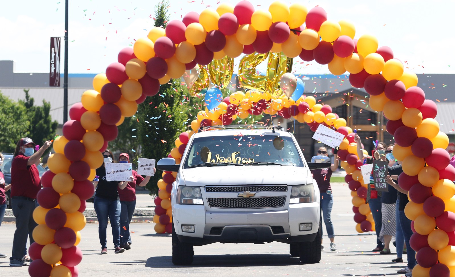 Car driving through an arch of balloons with confetti falling and people cheering