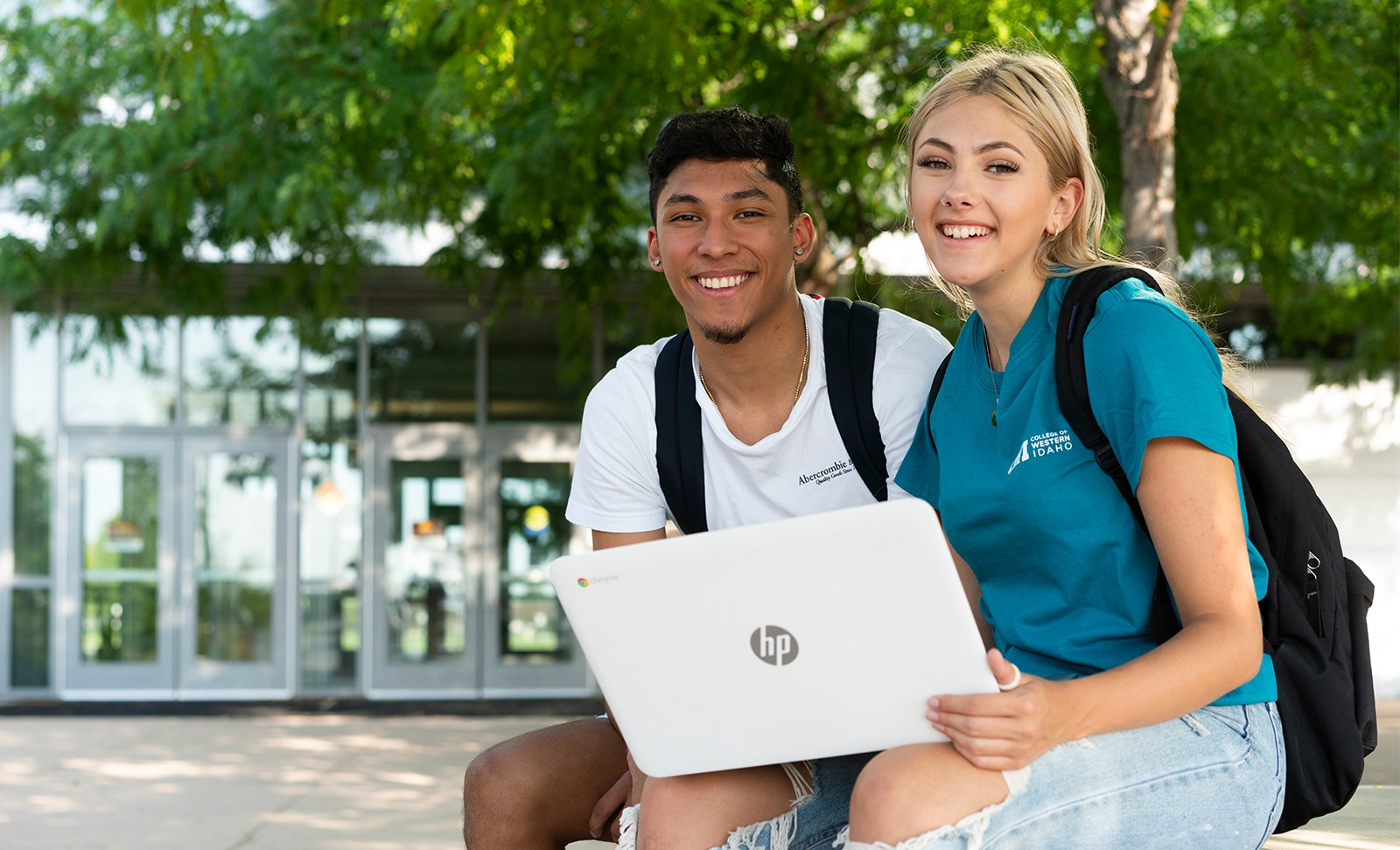 Students sitting outside Nampa Campus Academic Building with a laptop