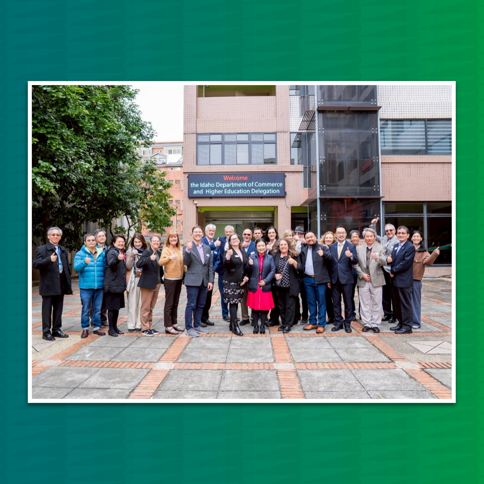 Group picture in front of a sign that states "the Idaho Department of Commerce and Higher Education Delegation" | Green backdrop