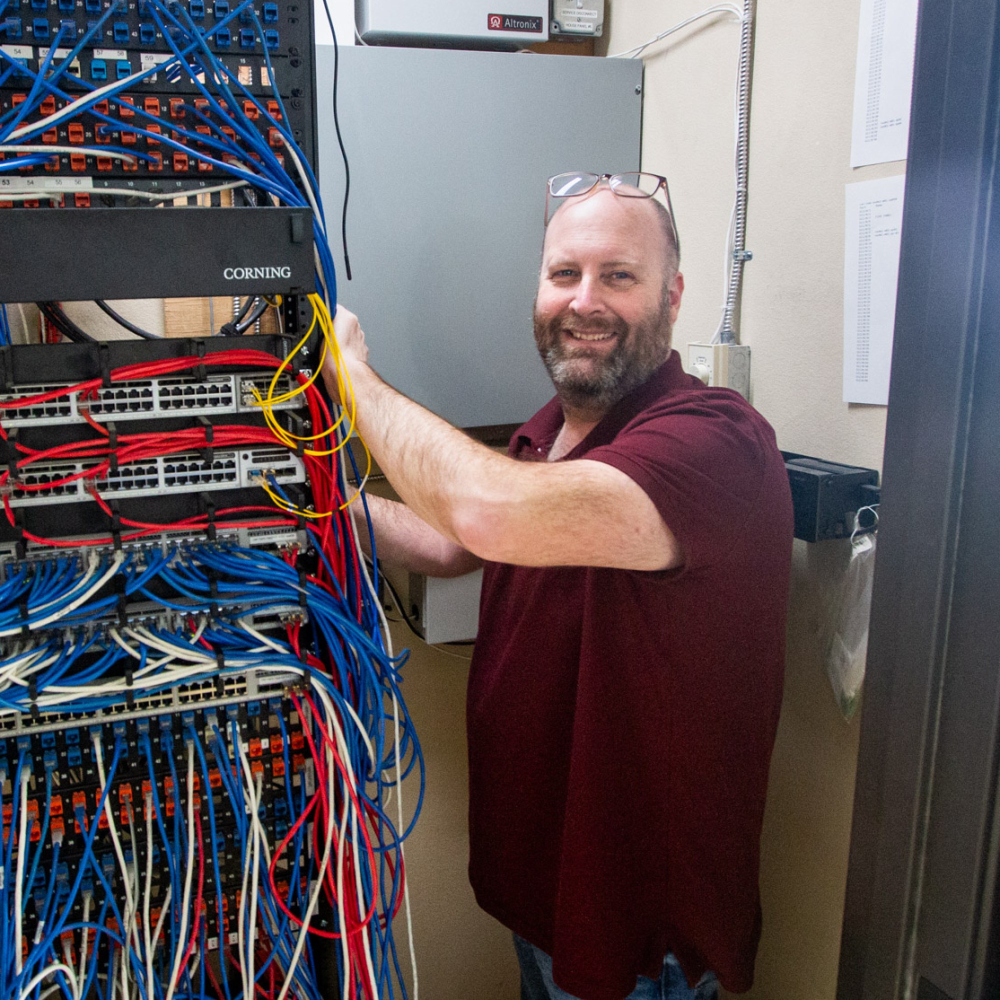 A portrait of William Alworth standing in a telcom closet surrounded by wires and ethernet cables.