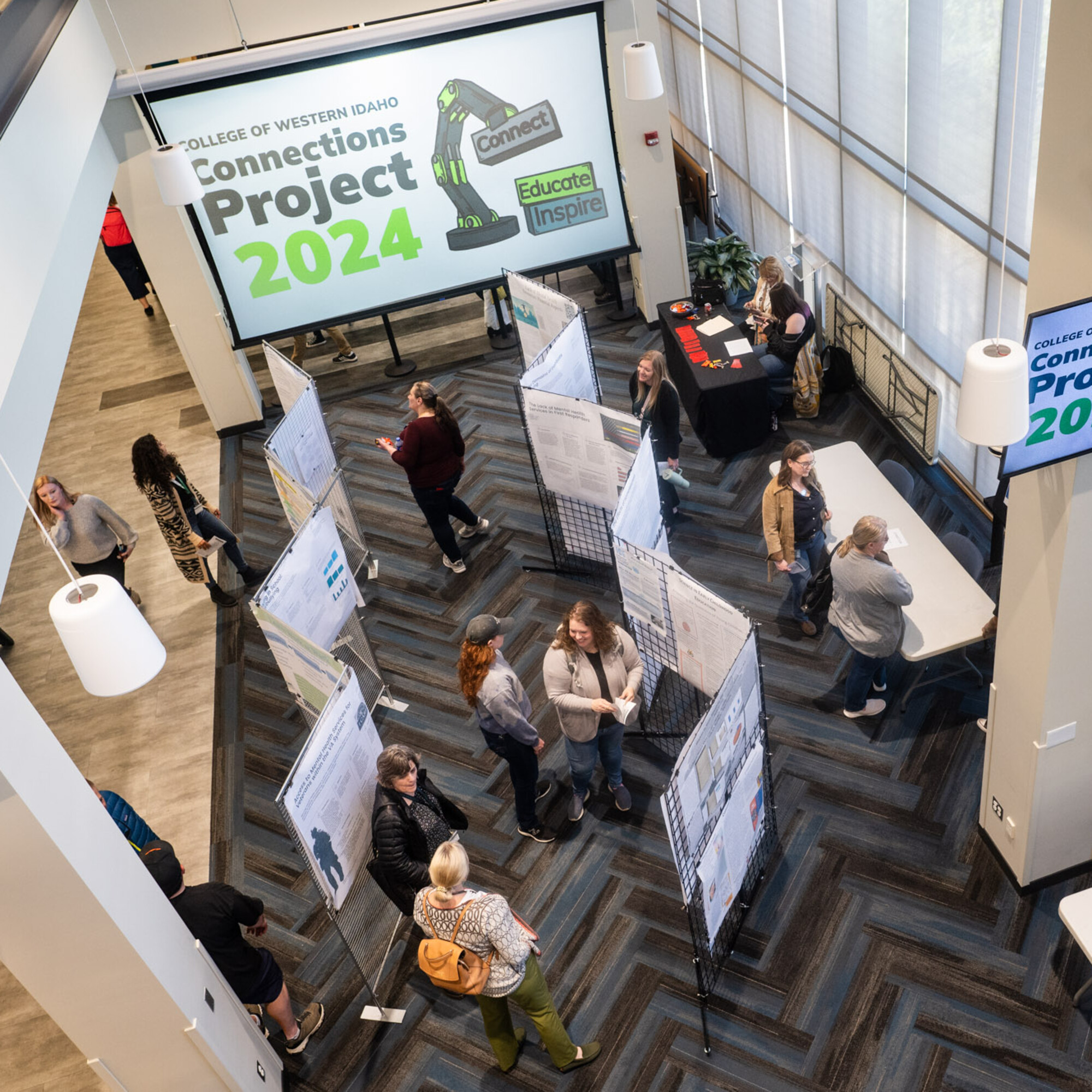 Students and members of the community browse research posters at an event. Screens display "Connections Project 2024."