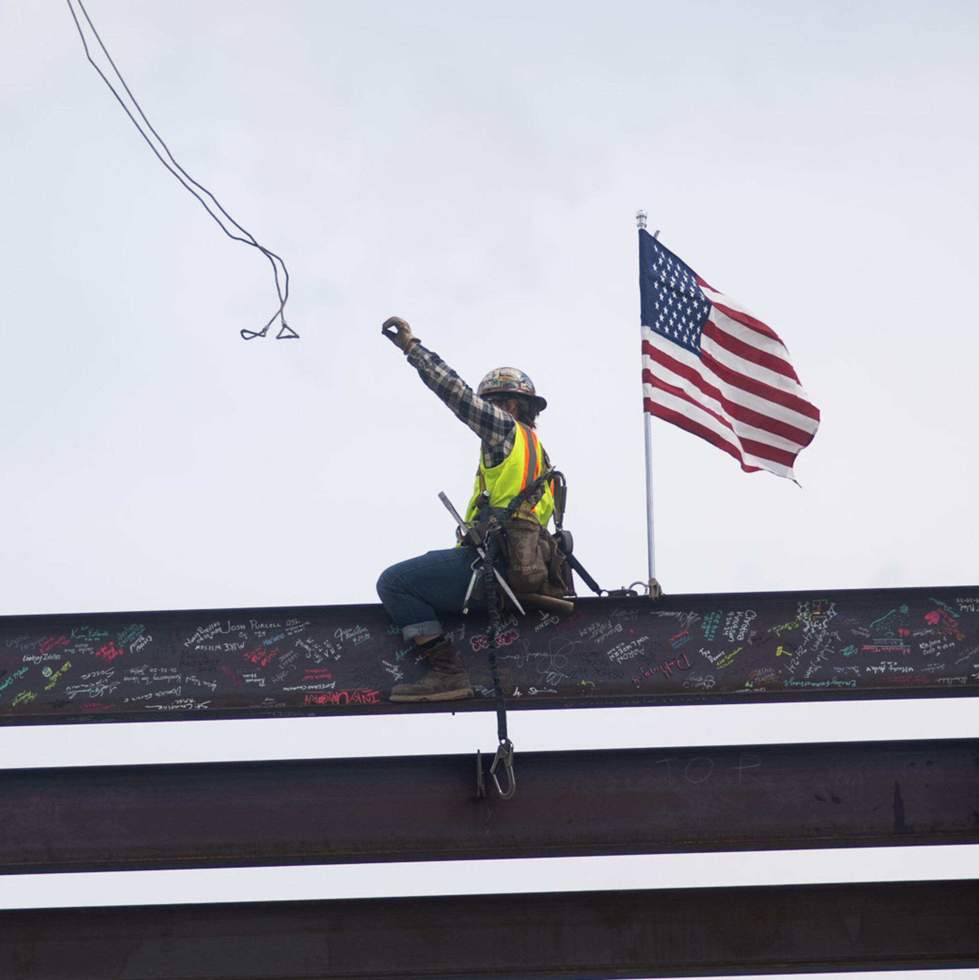 A construction worker throws off a wire attached to a crane that just lowered a beam onto a building's frame.