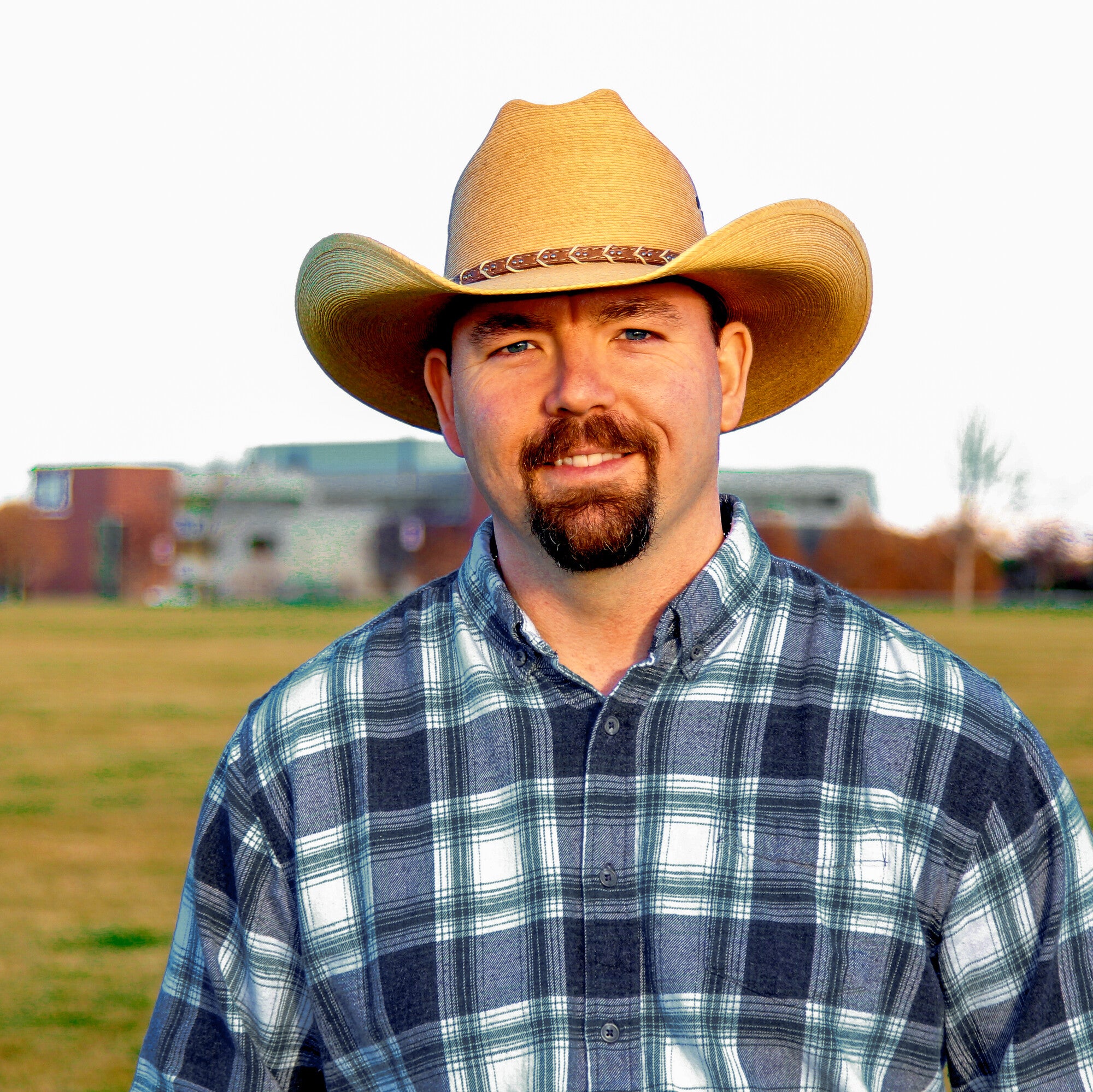 Man in cowboy hat in field with building behind him