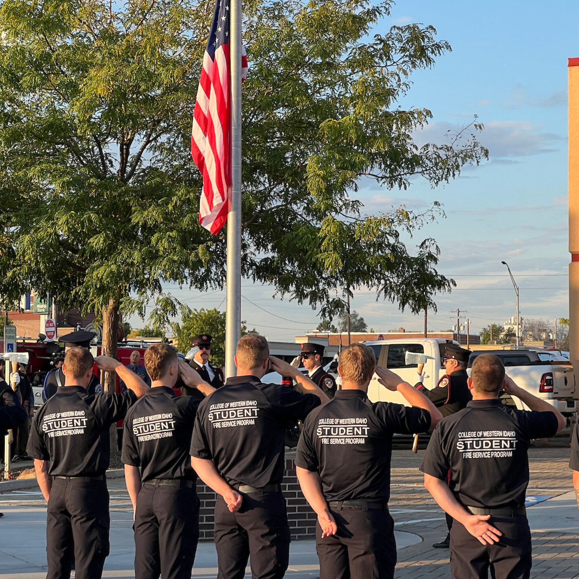 CWI Fire Service Program students saluting the American flag during a ceremony, with uniformed firefighters standing nearby.