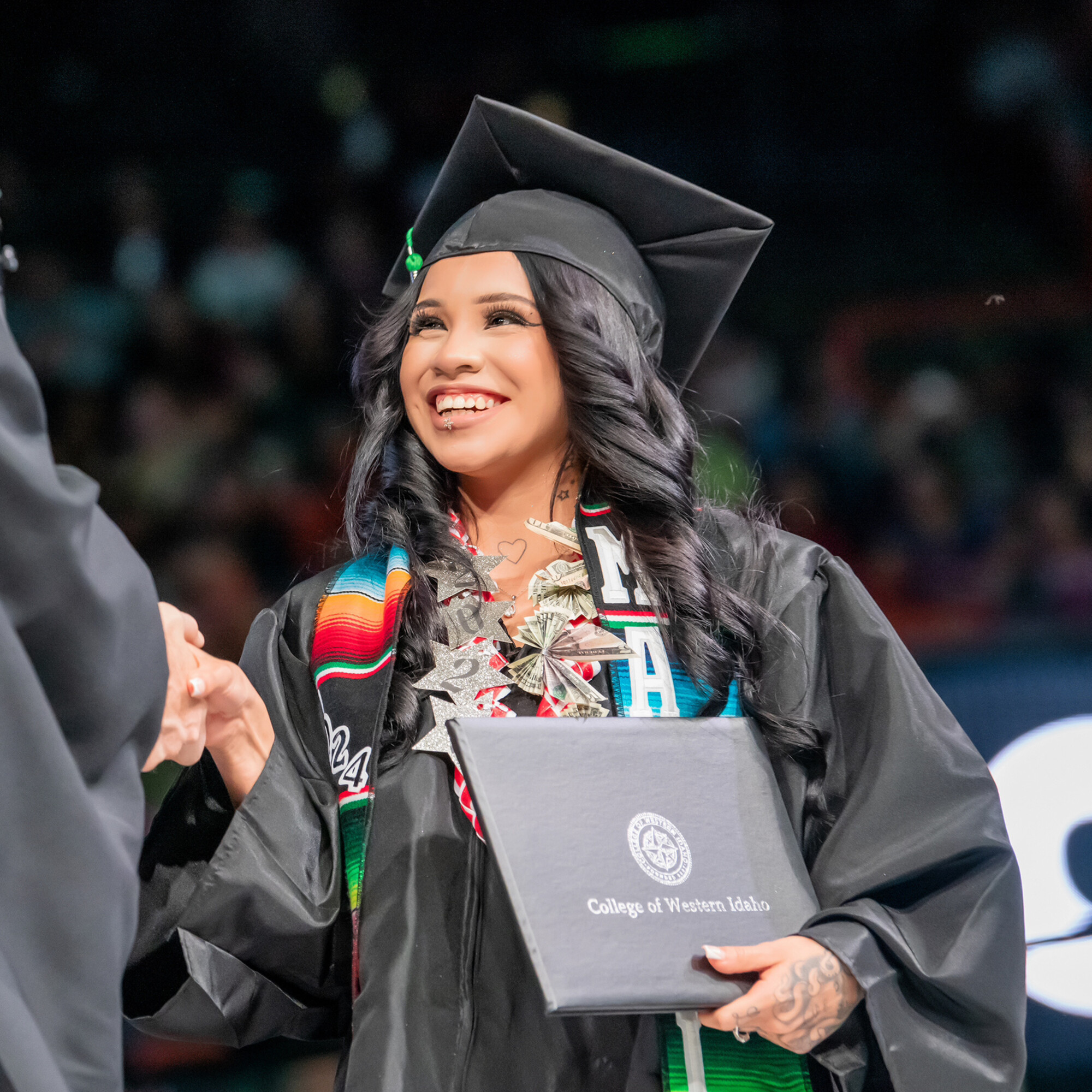 A student graduate in cap and gown accepts her degree with a handshake.