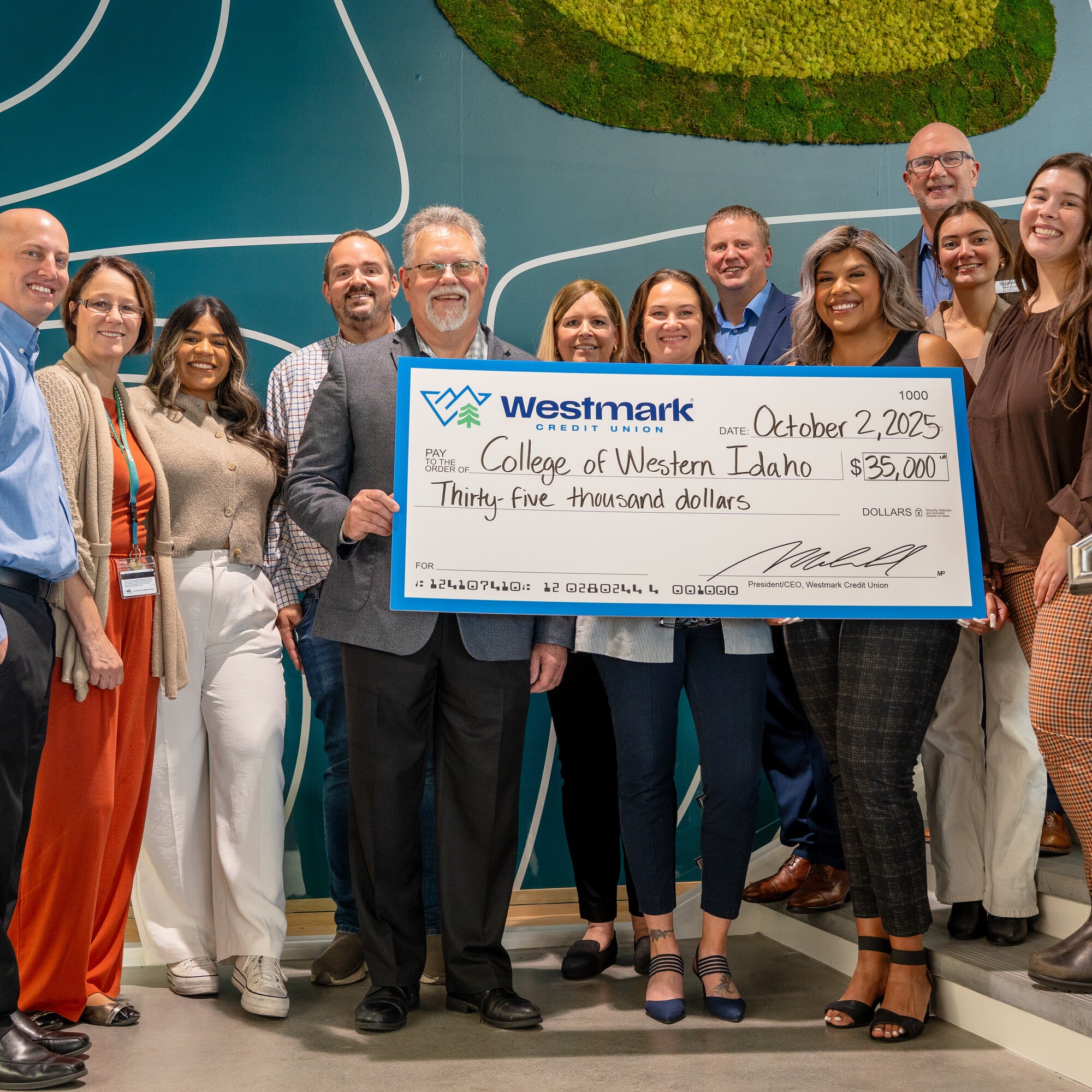A group of people stand on a staircase smiling and holding a large ceremonial check