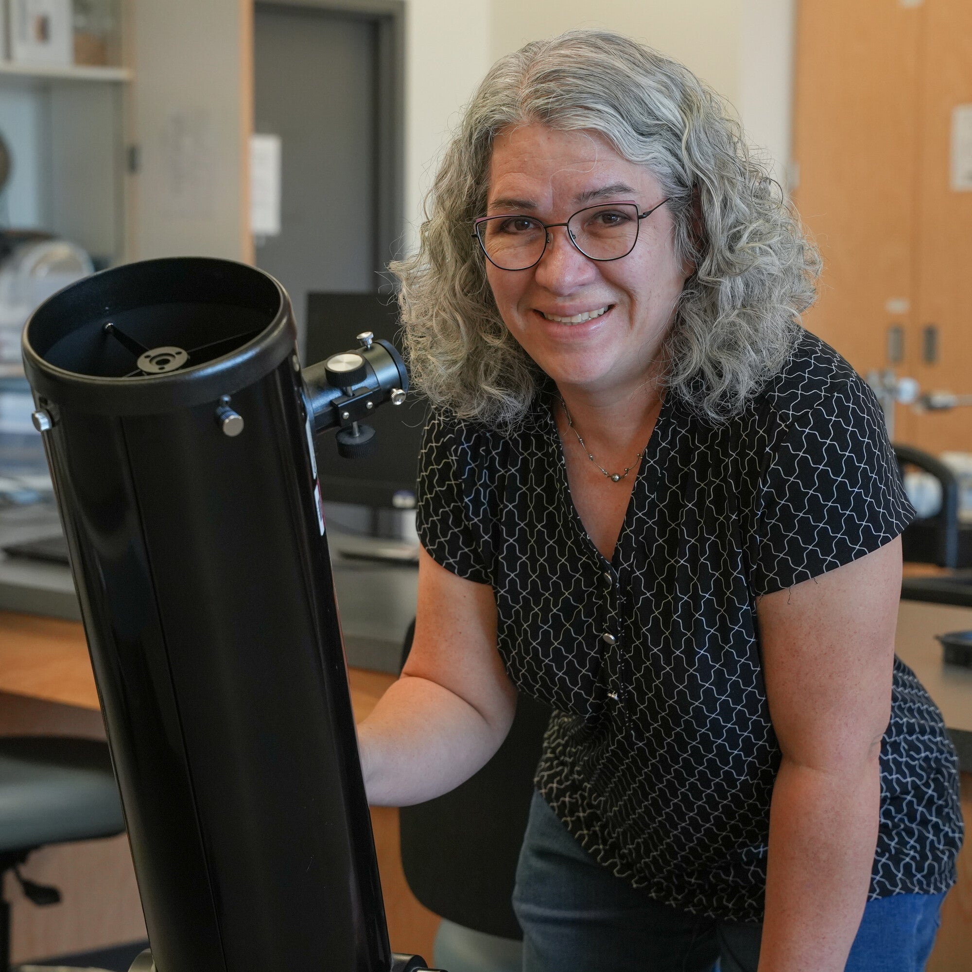 Stephanie Sevigny posing next to telescope in science lab