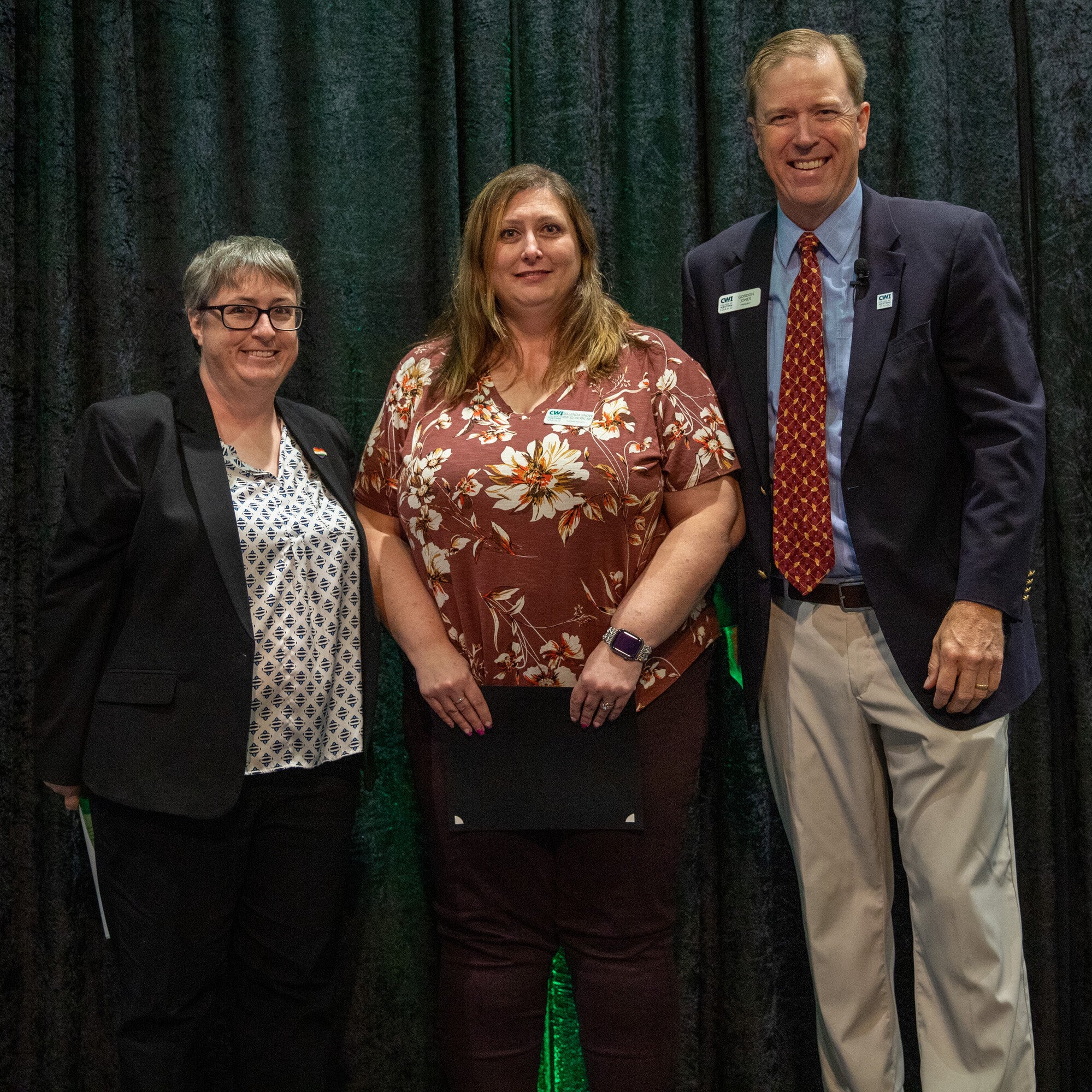 Three people stand in front of a curtain