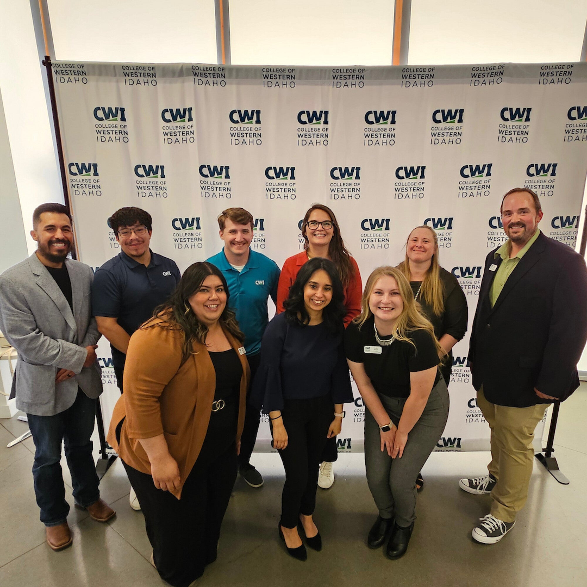 Ten individuals pose together, smiling in front of a CWI step-and-repeat backdrop at a campus event.