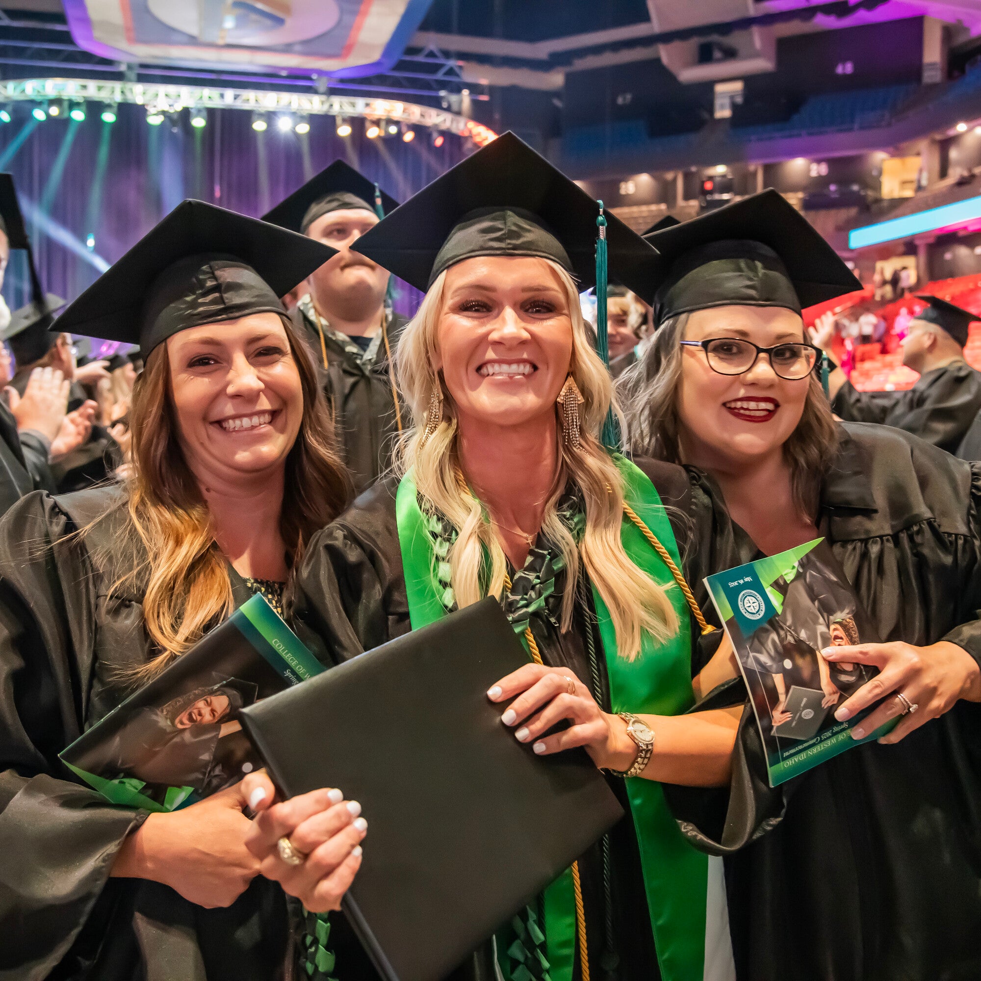 Three people with diplomas and in cap and gowns