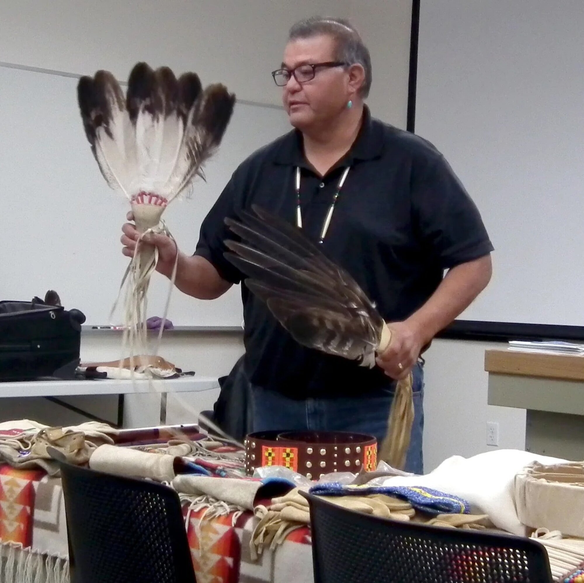 A Native American man demonstrates traditional ceremonial pieces in front of a class.