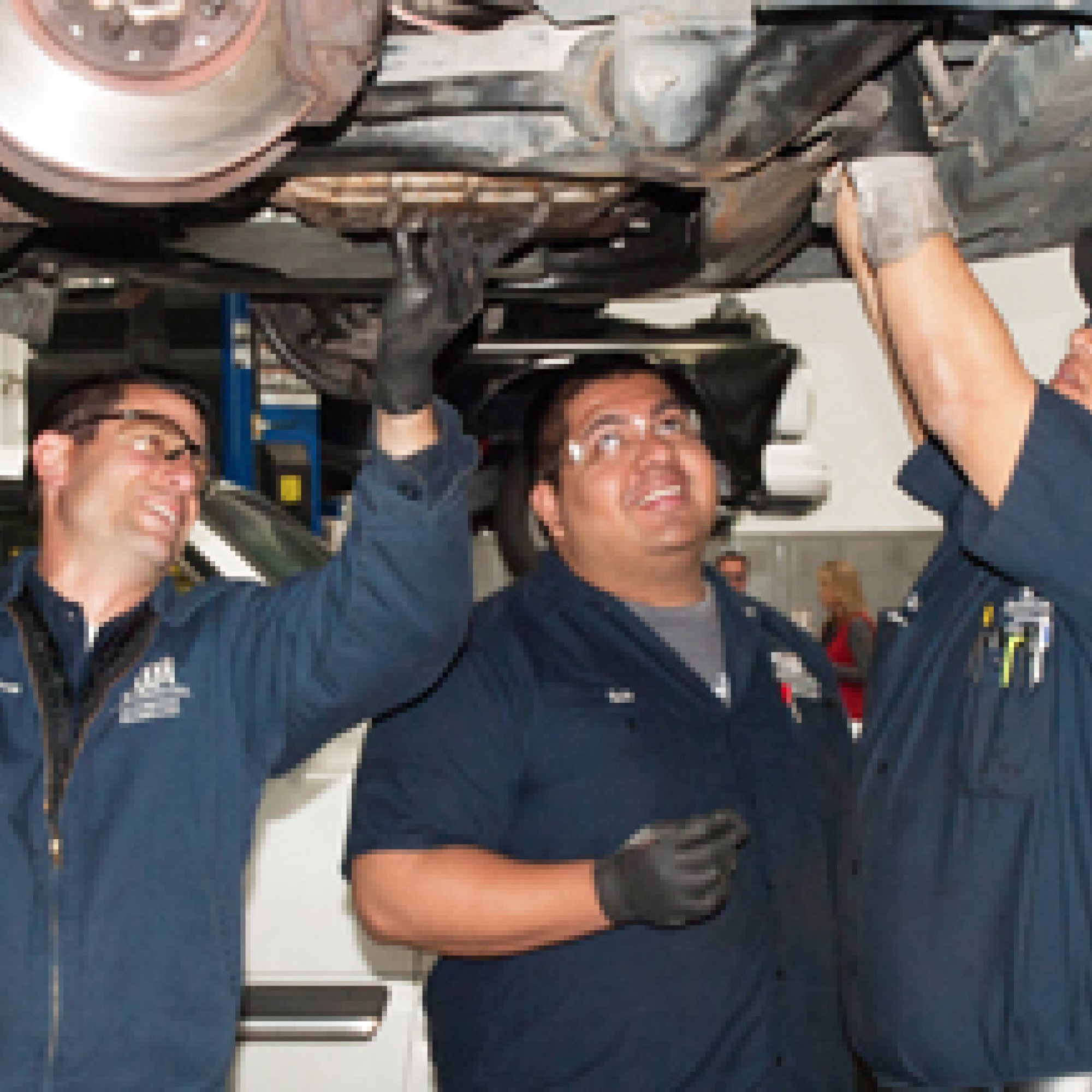 Three students working under a vehicle in the auto class.