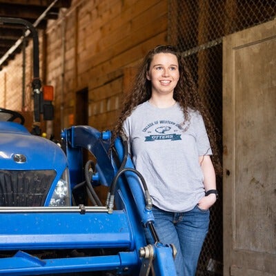 A student smiles next to a blue tractor.