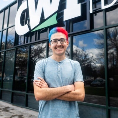 A student stands smiling in front of a building.