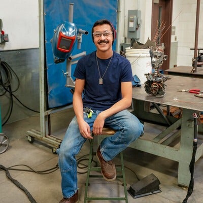 Person sitting on a stool, next to desk and welding tools