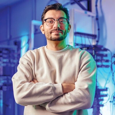 A man stands smiling with arms folded in front of server racks.