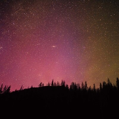 A photo of the night sky showing stars behind a silhouetted mountain top. 