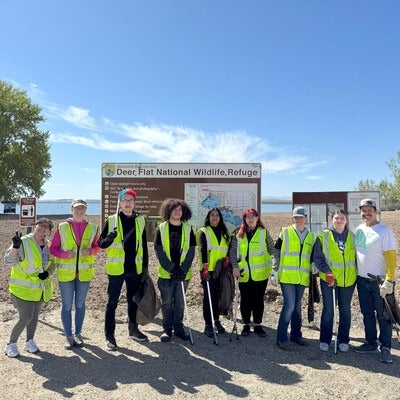 A group of volunteers pose at a park holding trash bags and rakes.