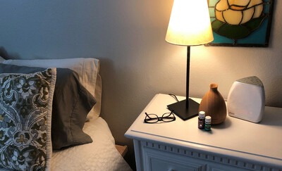 Nightstand next to a bed with glasses, a lamp, and essential oils on it.