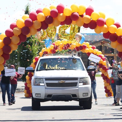 Car driving through an arch of balloons with confetti falling and people cheering