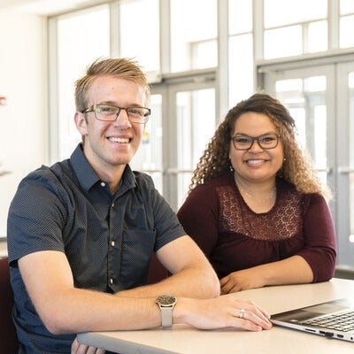 Two students sitting at a desk with a laptop on campus