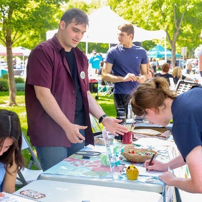 A student signs up for a club at a table display during an outdoor resource fair.