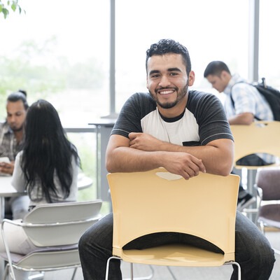 CWI student sitting backwards in a chair smiling with students studying.