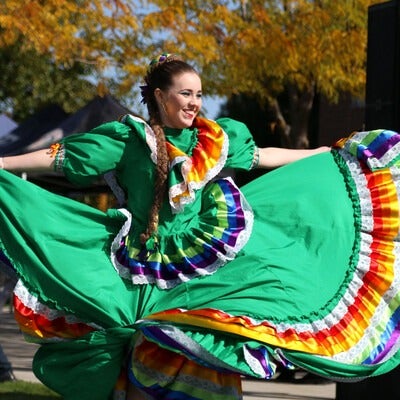 A dancer in traditional Hispanic dress dances at an outdoor event.