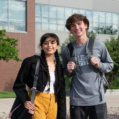 Two students with bags standing outside building