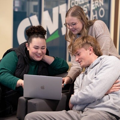 Three people sitting on a couch looking at a laptop