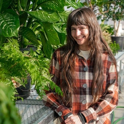 Student stands in greenhouse in front of several plants