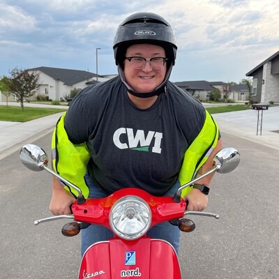 Faculty member, Maia Kelley, riding a moped and wearing a newly-branded CWI shirt