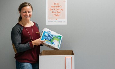 Woman standing by donation box holding donation of toilet paper