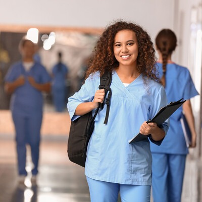 Smiling nursing student in scrubs, holding a binder and a backpack