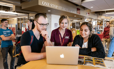Students and an advisor at a laptop surrounded by other students near One Stop Student Services