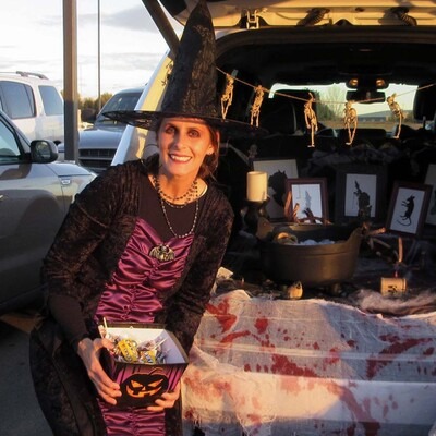 Woman dressed as a witch sitting in a decorated trunk and handing out candy