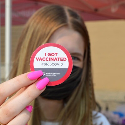 Woman holding up a sticker stating vaccination status