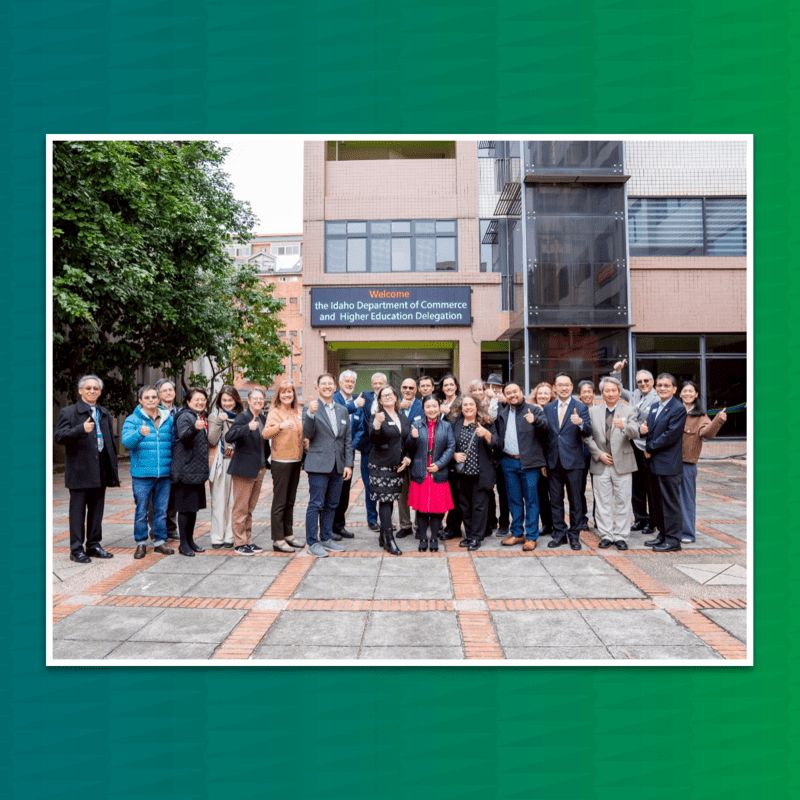 Group picture in front of a sign that states "the Idaho Department of Commerce and Higher Education Delegation" | Green backdrop