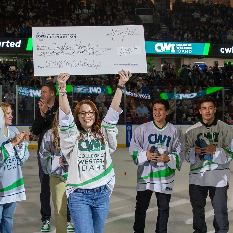 A smiling scholarship winner holds up a big $1000 check on the ice of a hockey rink.