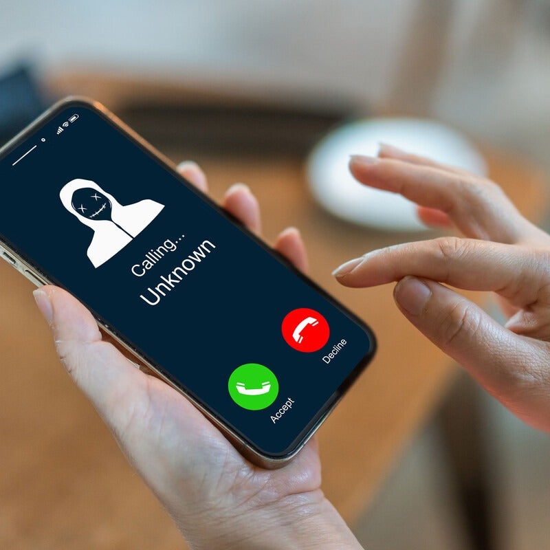 An image of a person holding a phone that displays an unknown caller.