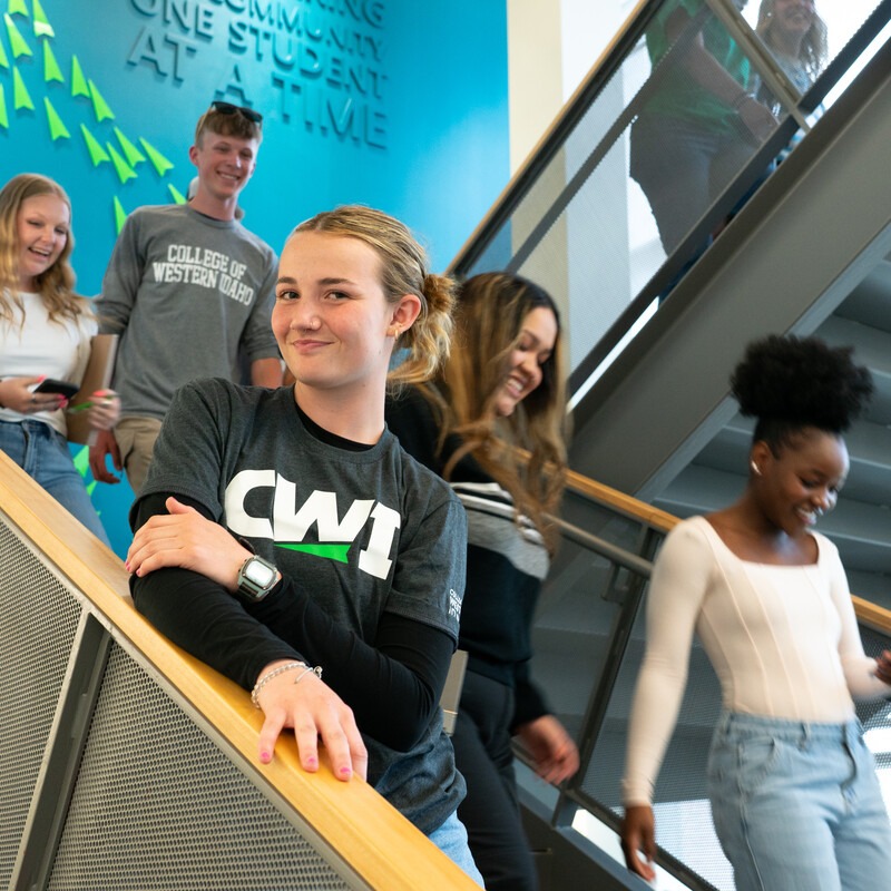Group of students walking down the stairs on campus, one girl looking at the camera wearing a CWI shirt