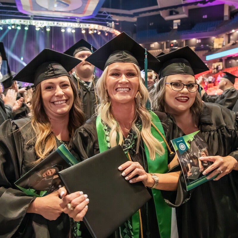 Three people with diplomas and in cap and gowns