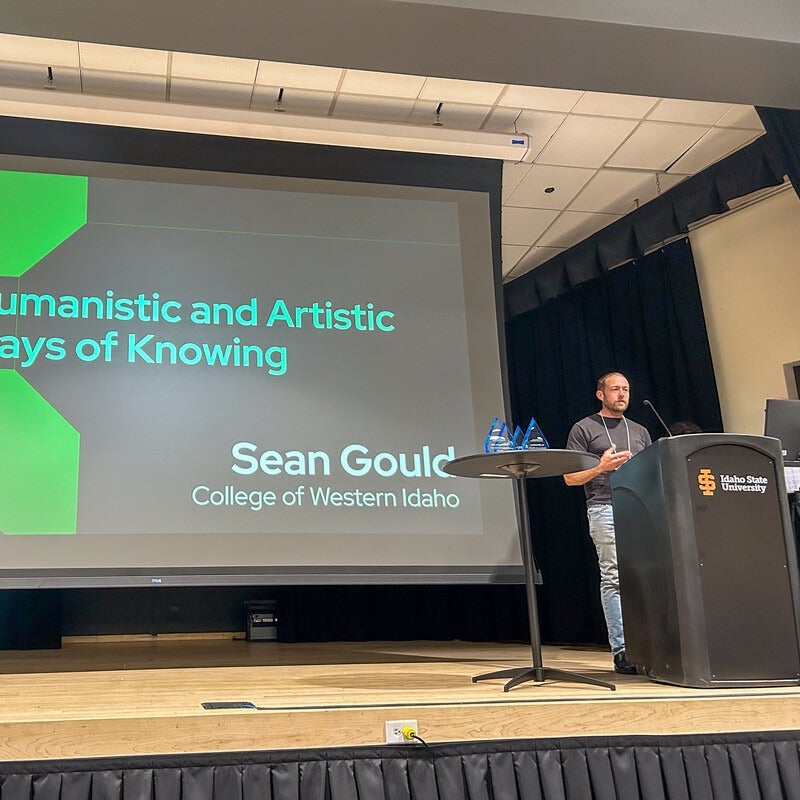 Sean Gould presenting on stage with projector screen behind them