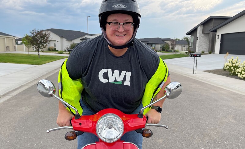 Faculty member, Maia Kelley, riding a moped and wearing a newly-branded CWI shirt