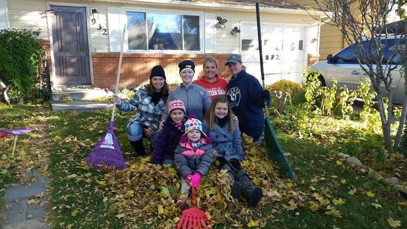 Employees raking up community event posing with leaves and rakes